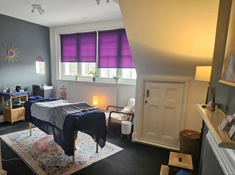 A treatment couch beneath purple window blinds in a bright massage room at The Treatment Rooms.